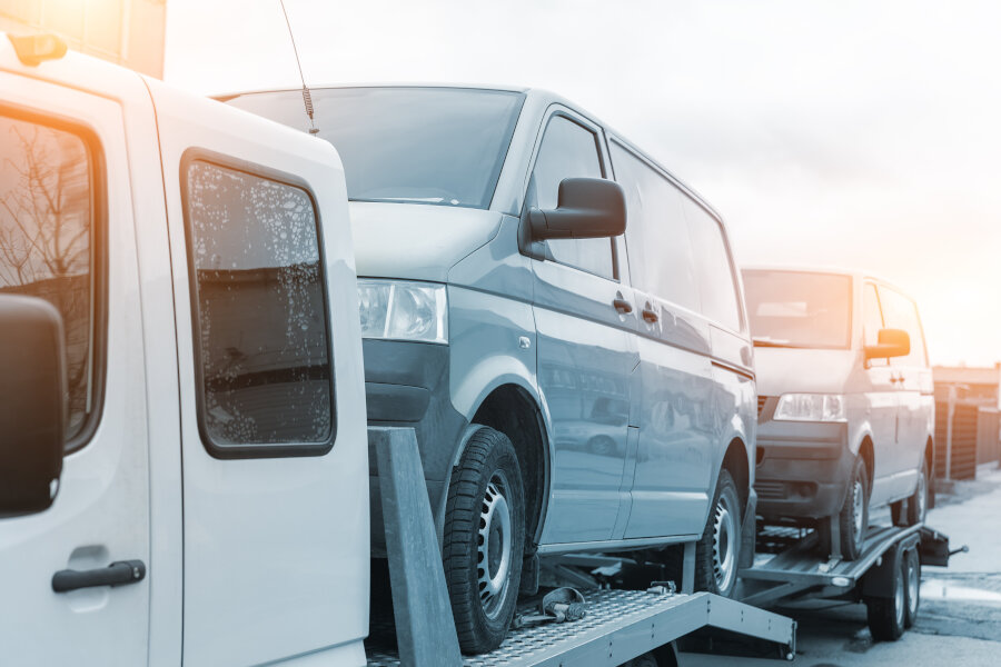 White Small Cargo Truck Car Carrier Loaded With Two Yellow Van Minibus On Flatbed Platform And Semi Trailer Tow On Roadside Highway Road